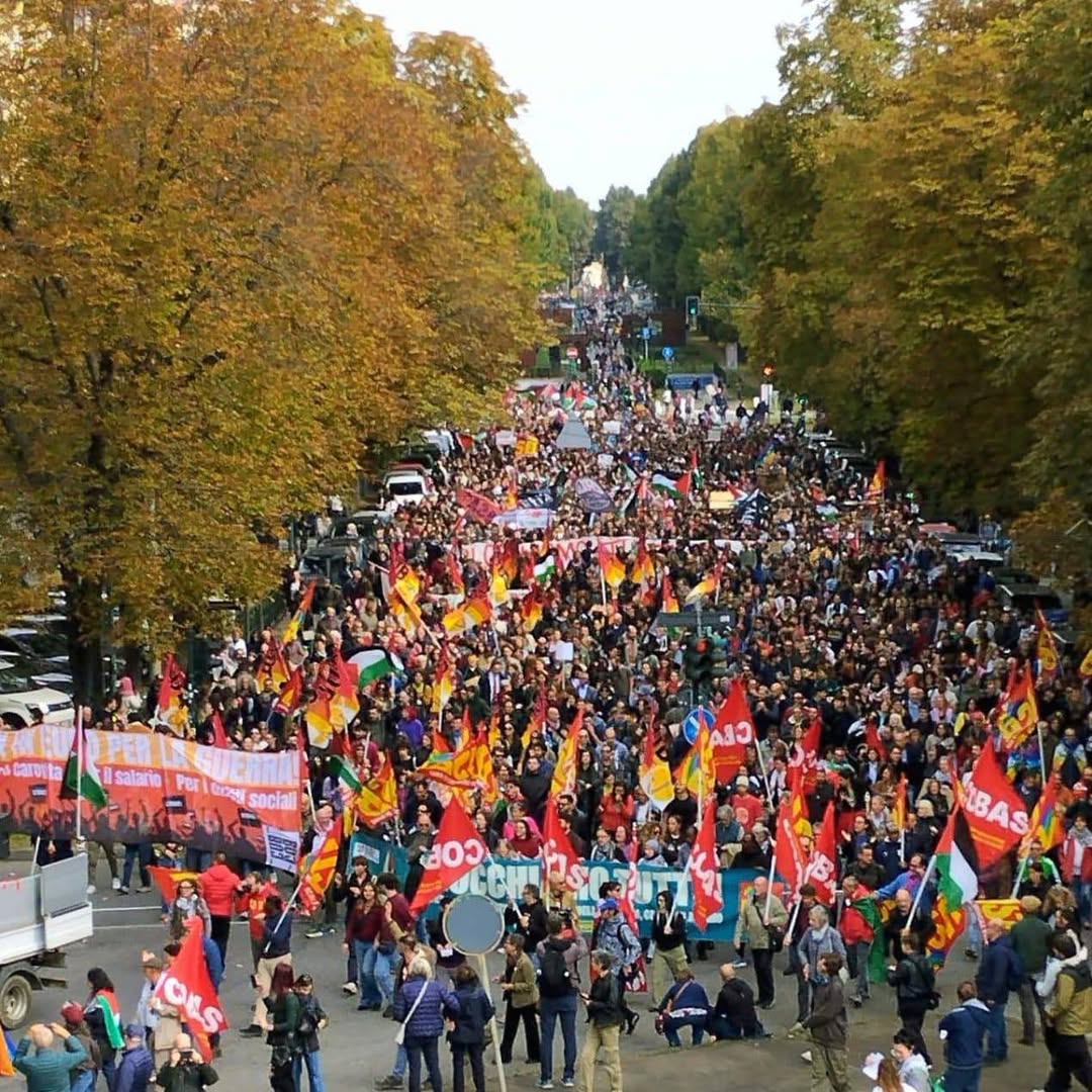 Gran manifestación en una avenida arbolada, con una multitud de personas que portan banderas rojas, amarillas y palestinas, en una protesta en Italia en solidaridad con Palestina.