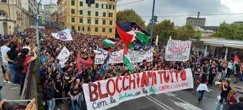 Multitud en protesta con una gran pancarta que dice “Blocchiamo tutto”, carteles y banderas en una calle de una ciudad italiana.