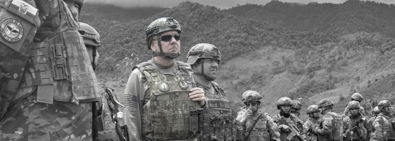 Grupo de militares con uniformes de camuflaje y chalecos tácticos en una zona montañosa; uno de ellos, en primer plano, lleva gafas oscuras y casco.