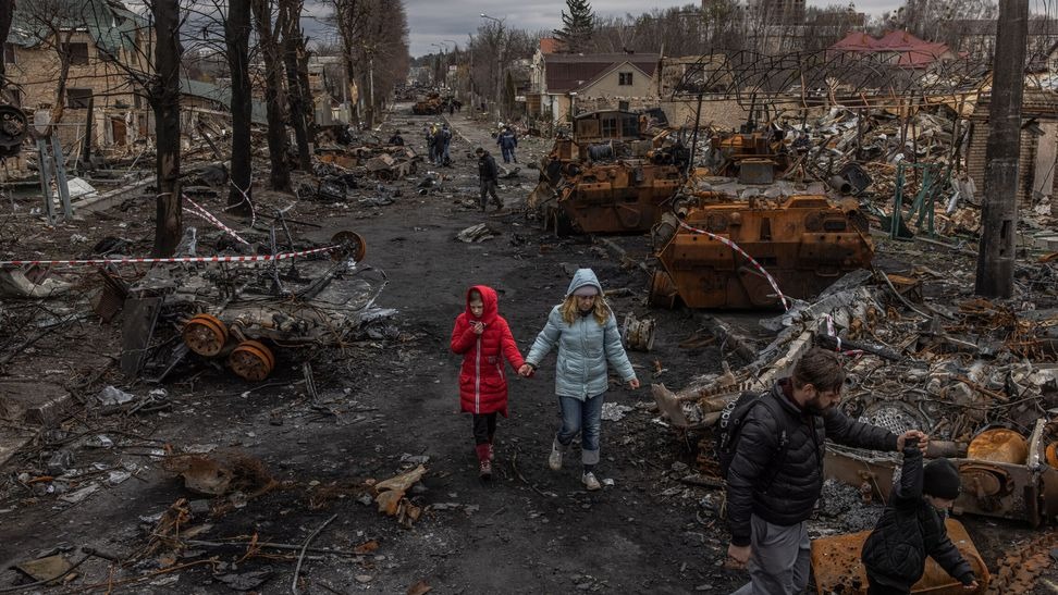 Personas caminan por una calle destruida con vehículos militares quemados y casas dañadas en Bucha, al norte de Kiev, después de la retirada de las fuerzas rusas.