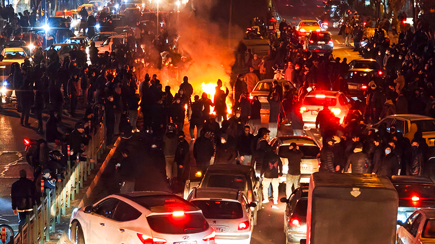 Personas durante una protesta nocturna en Irán, con vehículos detenidos y una fogata encendida en medio de la calle.